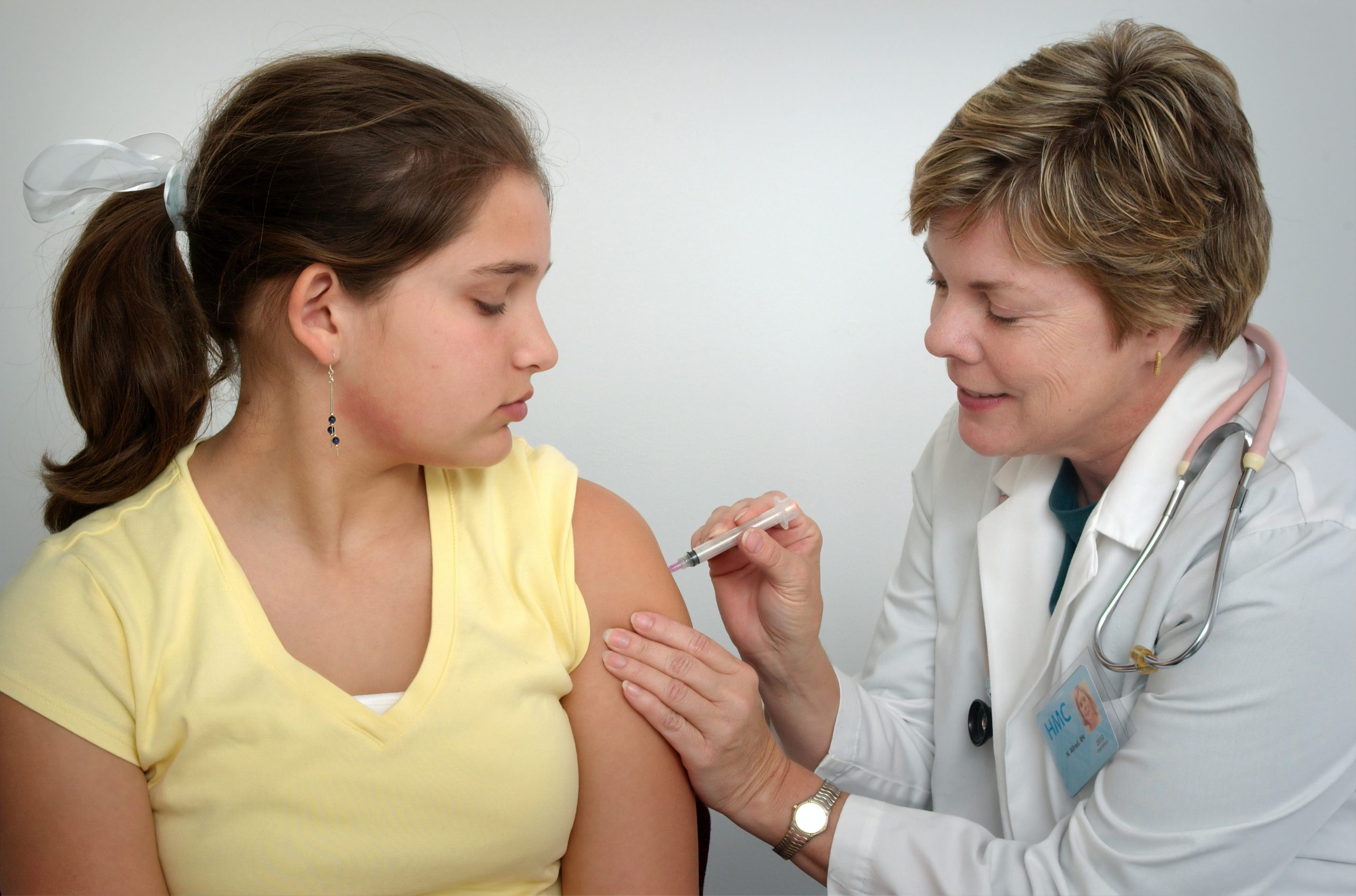 Woman injecting girl's right arm.