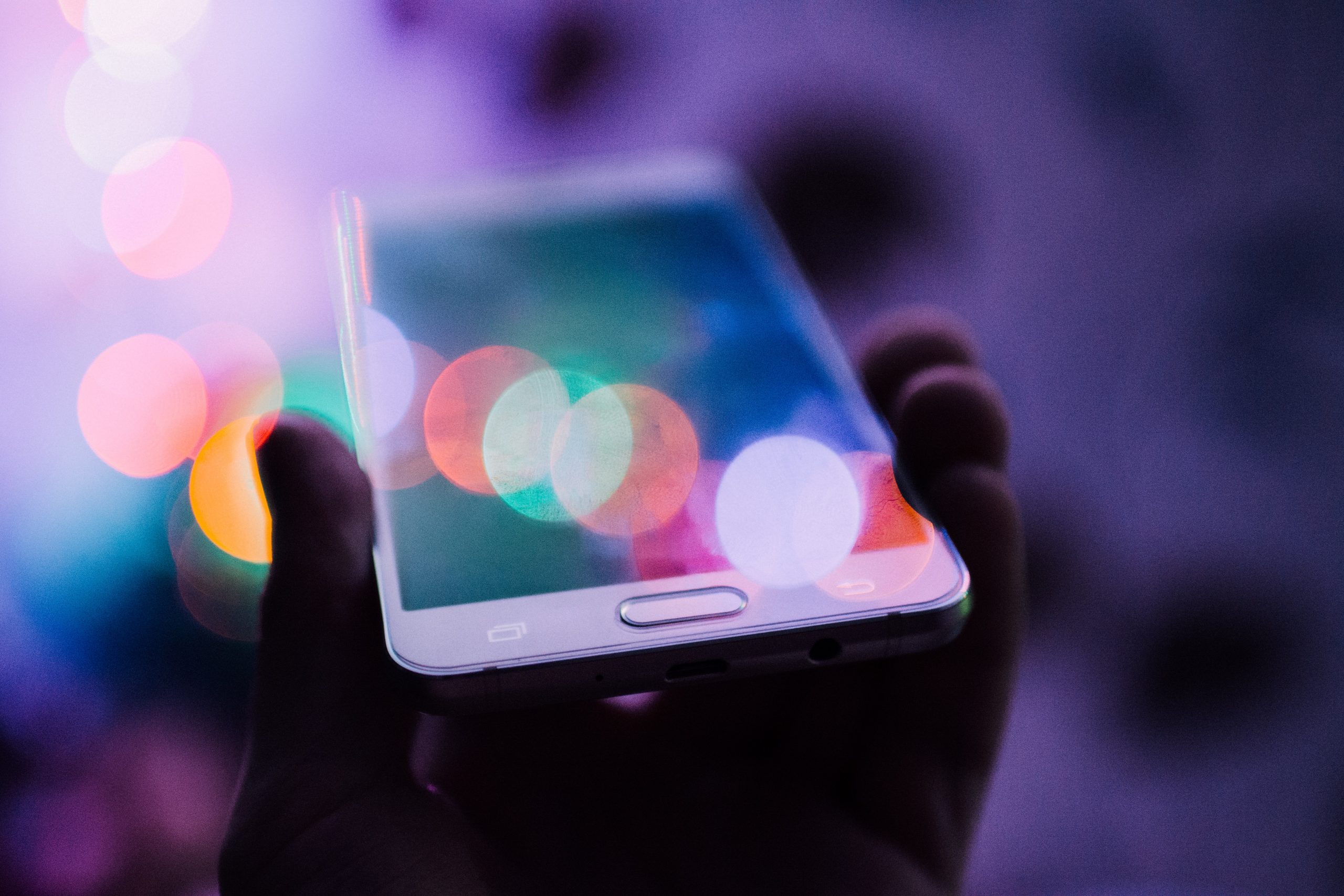 Photograph of hand holding smartphone, with blur of rainbow-like circles of light blurring on top