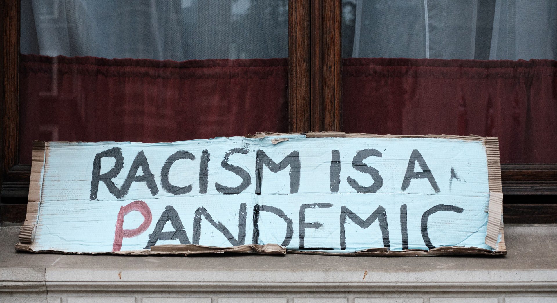 black and white sign written on cardboard that says "racism is a pandemic"
