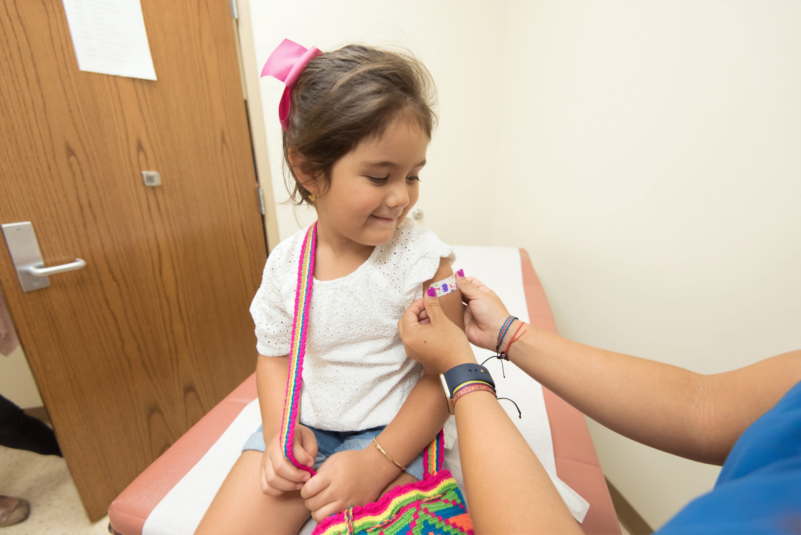 Young girl sits in doctors office and receives a bandaid on her arm from a nurse
