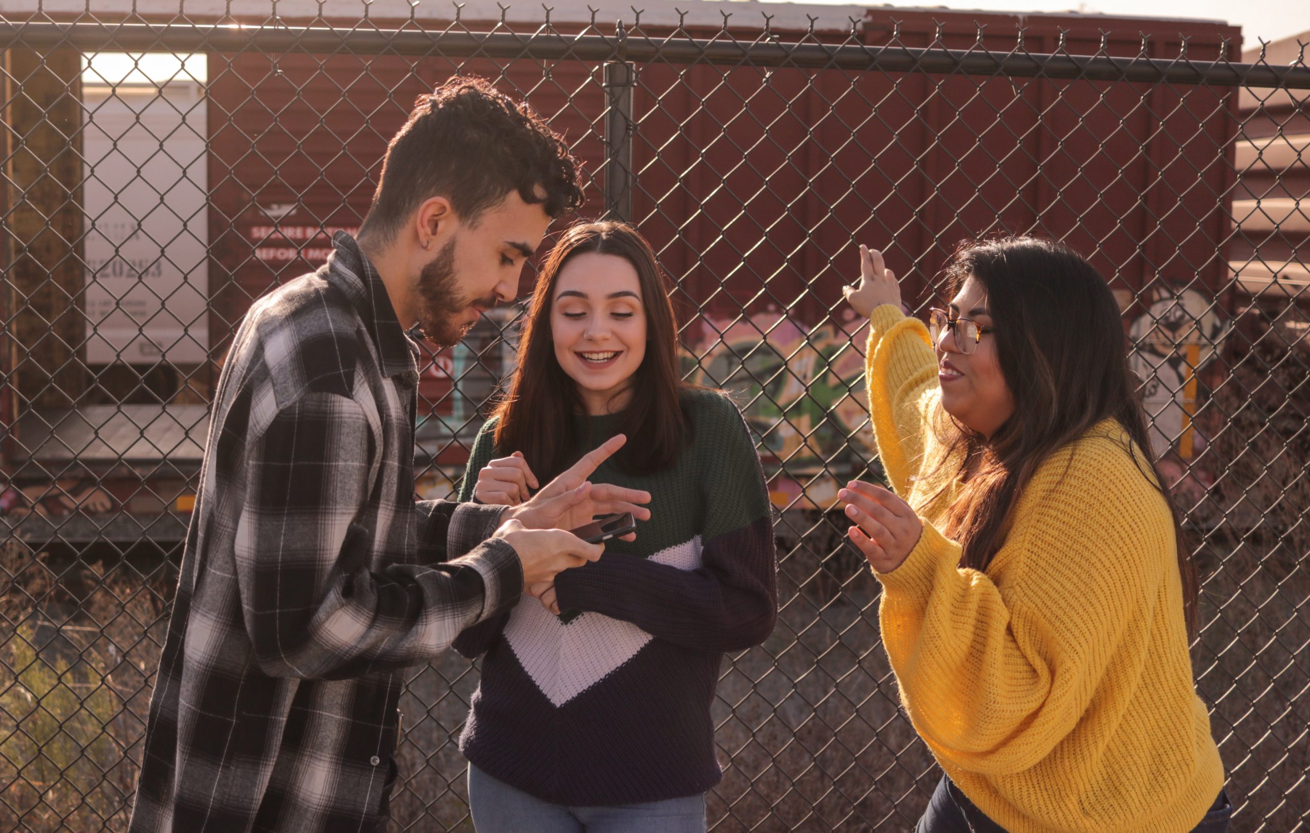 Three teens are leaning against fence and looking at a cellphone