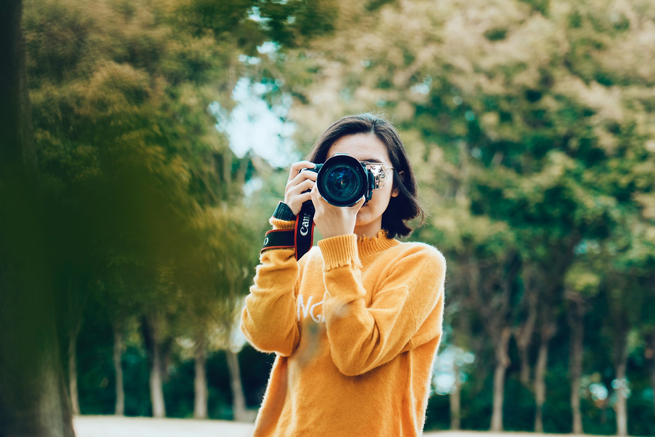 woman in a yellow sweater holding a DSLR camera outside