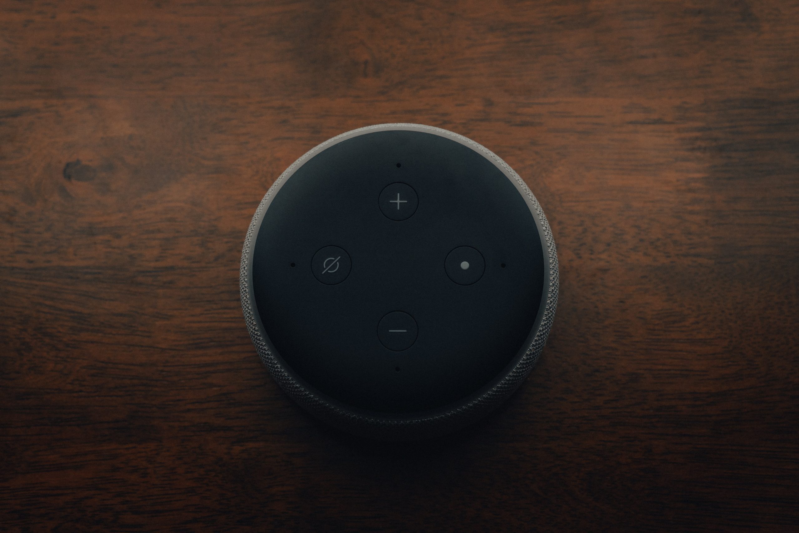 Amazon Echo Dot in black sitting on a dark wood table