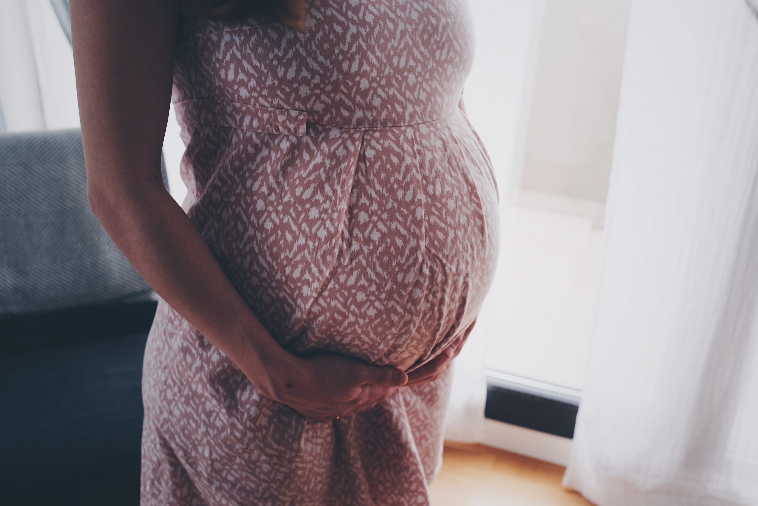 Image of a women in a patterned dress holding her pregnancy belly