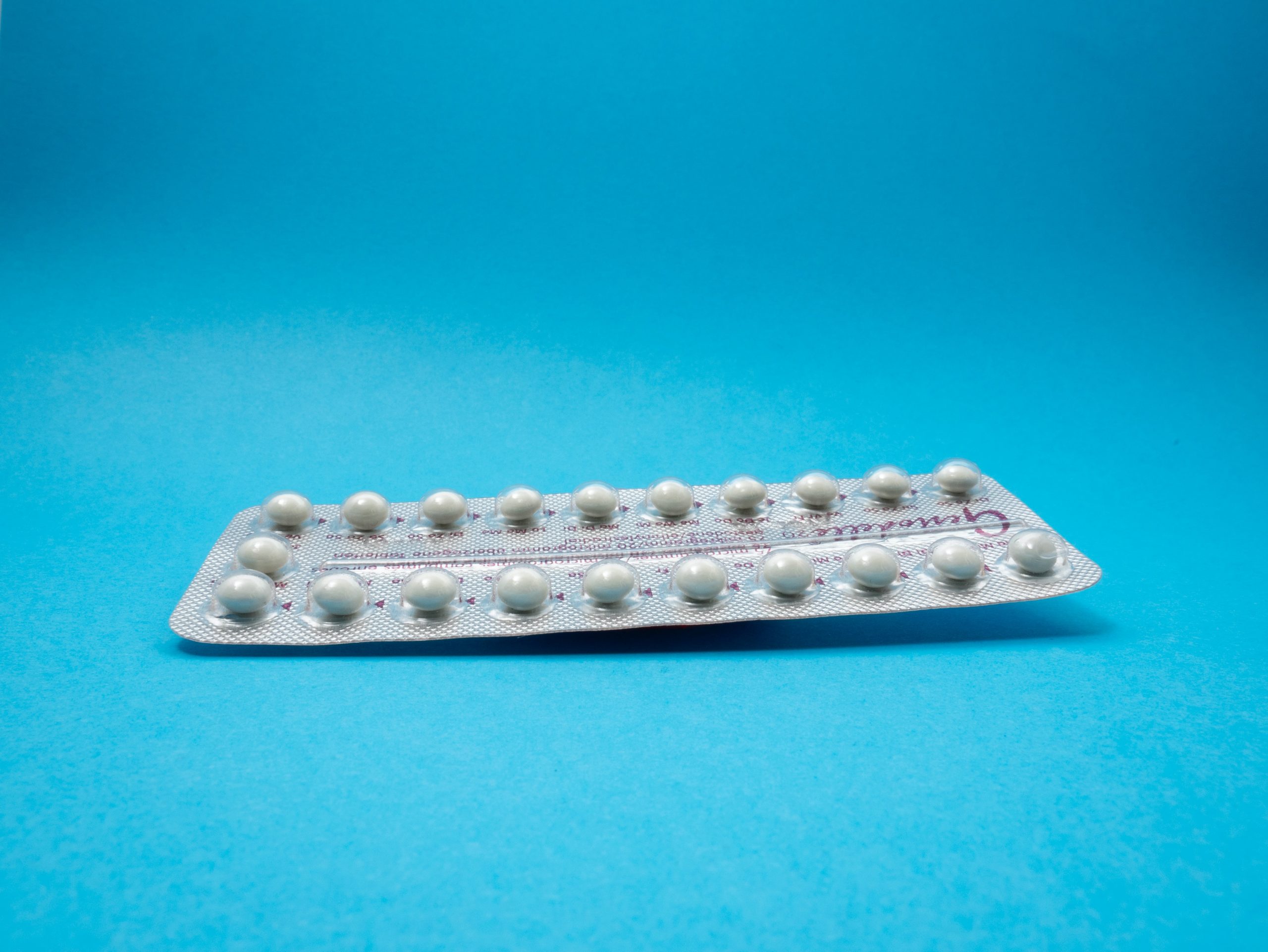 White birth control pill in wrapper on a blue background